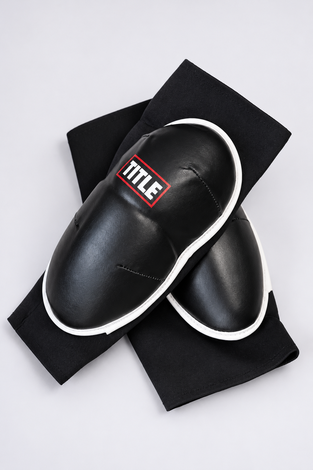 TITLE Clinch elbow guards crossed at an angle, black moulded leather pad with white edge over a stretch sleeve