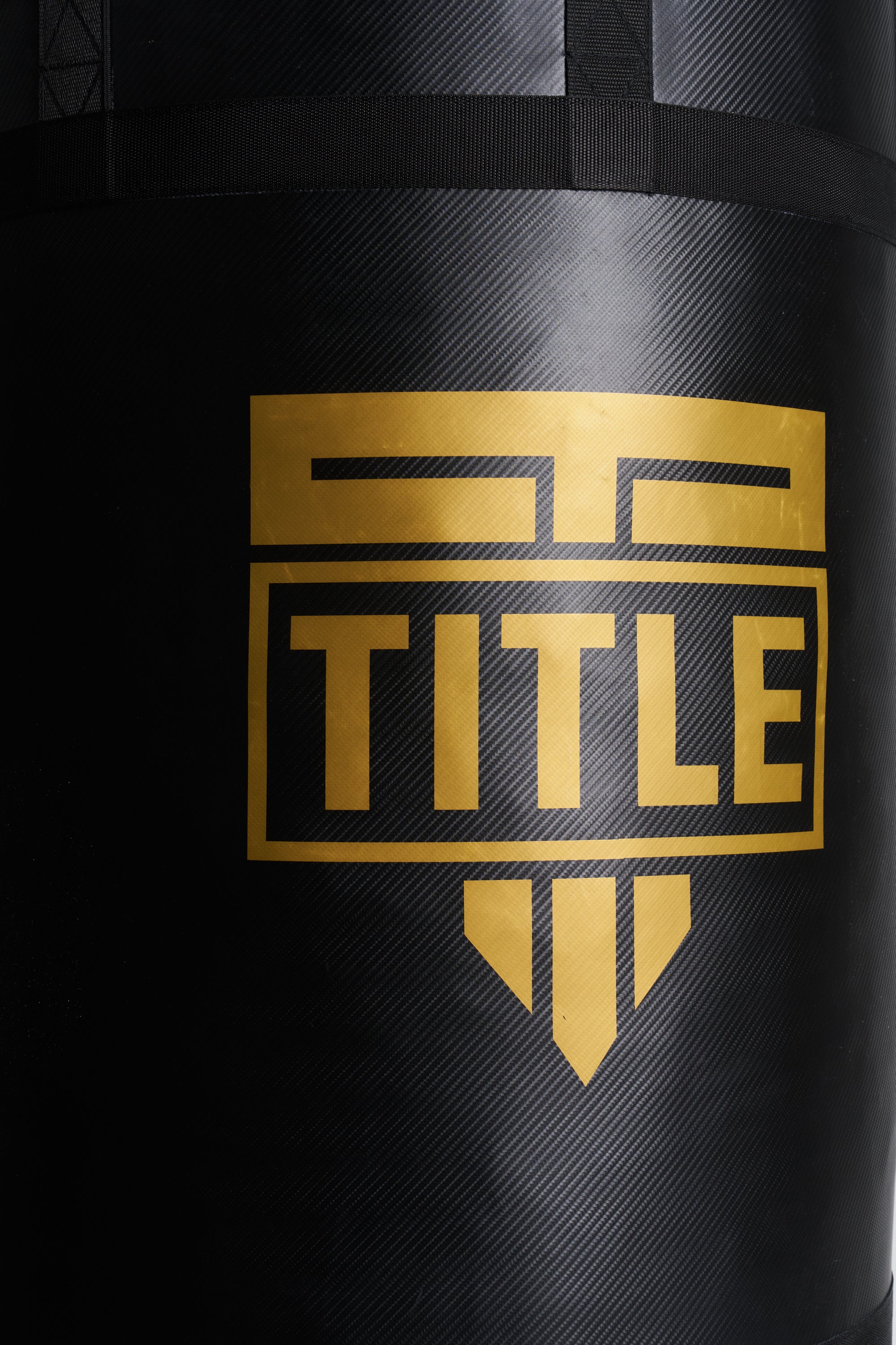 Close-up of a black heavy punching bag with a textured carbon-fiber-like finish and a large gold TITLE logo on the front.