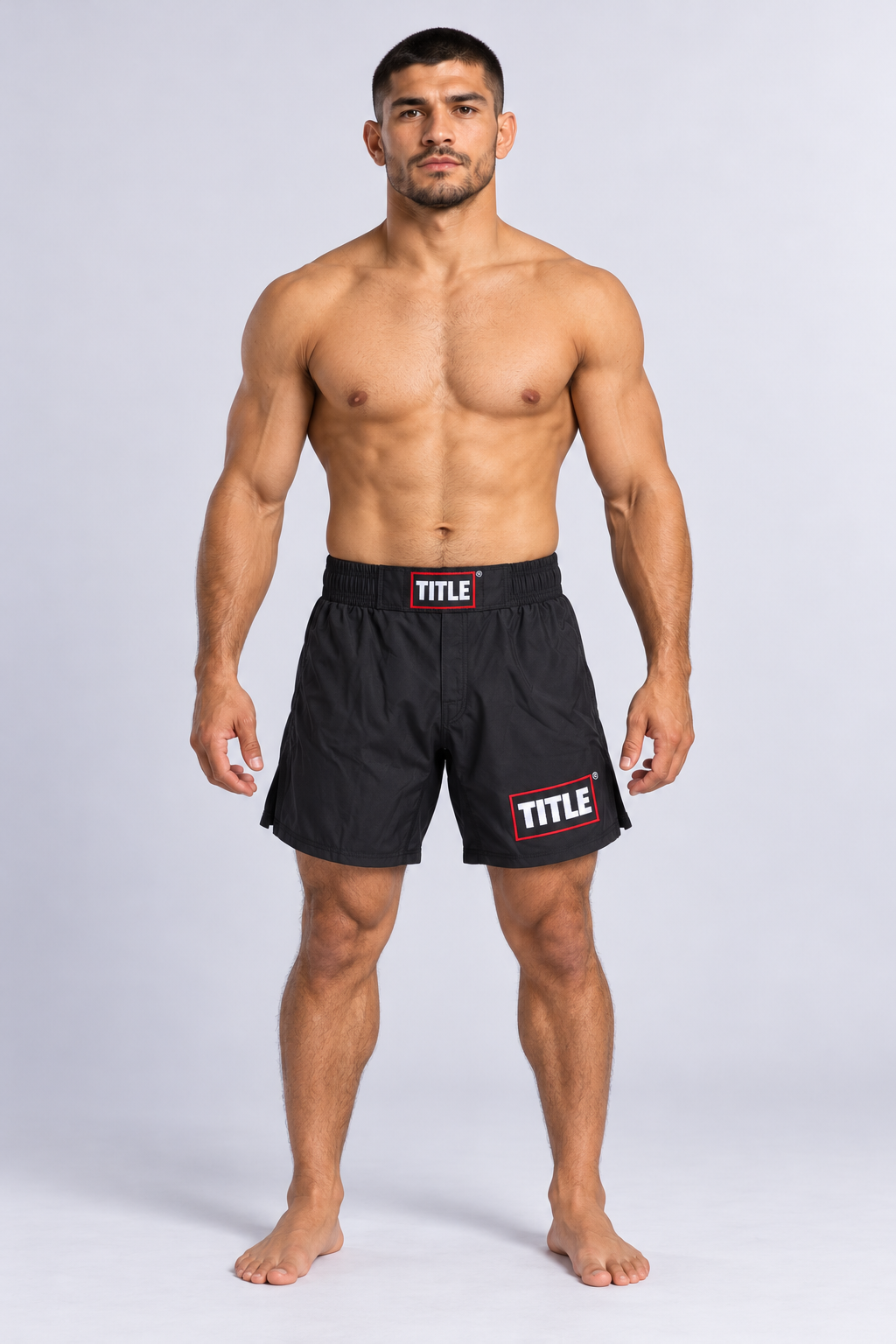 Athlete in TITLE Blackout black MMA shorts, front view with waistband patch, side splits and leg logo