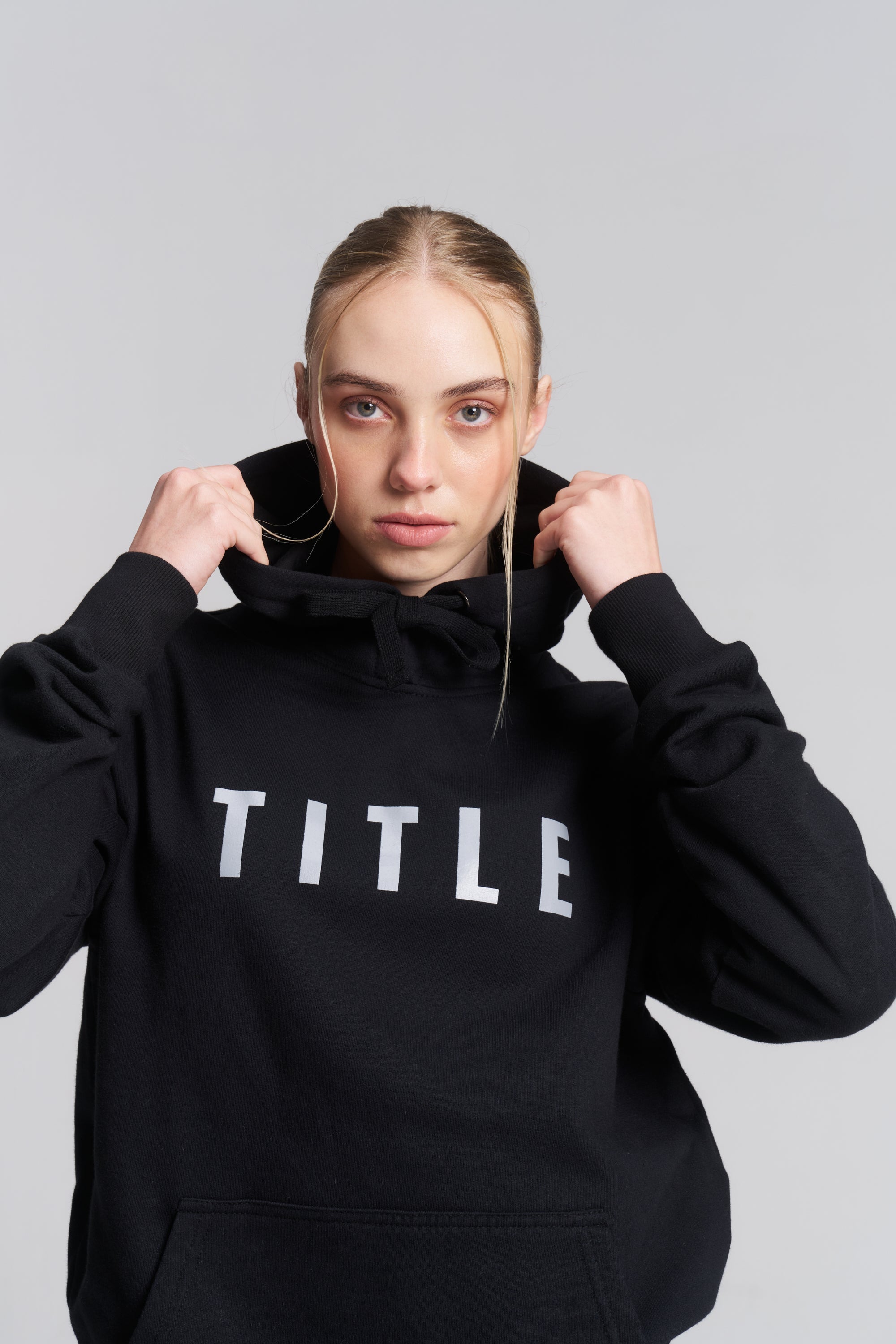 TITLE Boxing South Africa black cotton hoodie with grey chest logo worn by a woman pulling up the hood