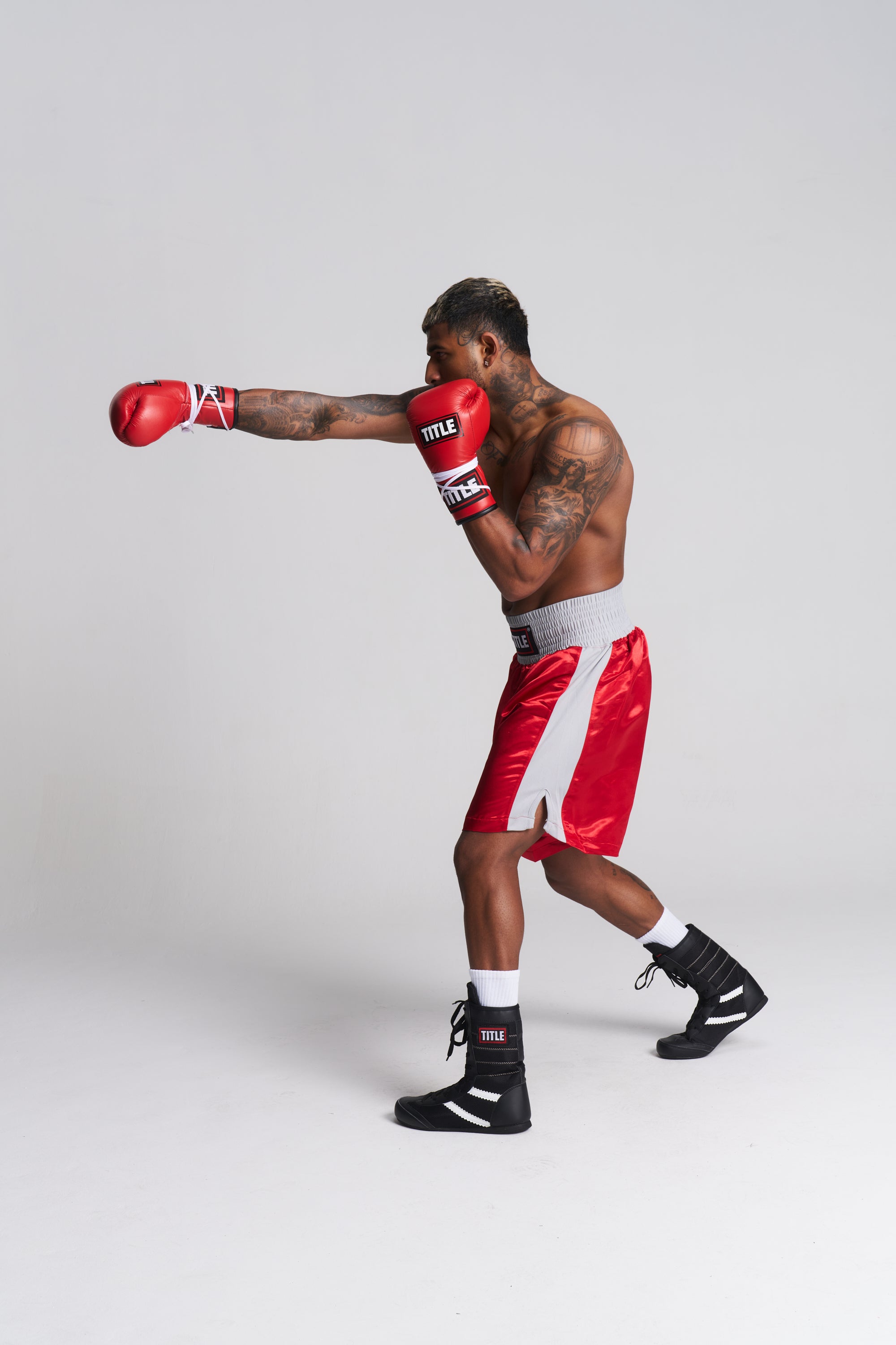 TITLE Boxing South Africa high-top black boxing boots worn by a tattooed boxer throwing a punch in red boxing shorts