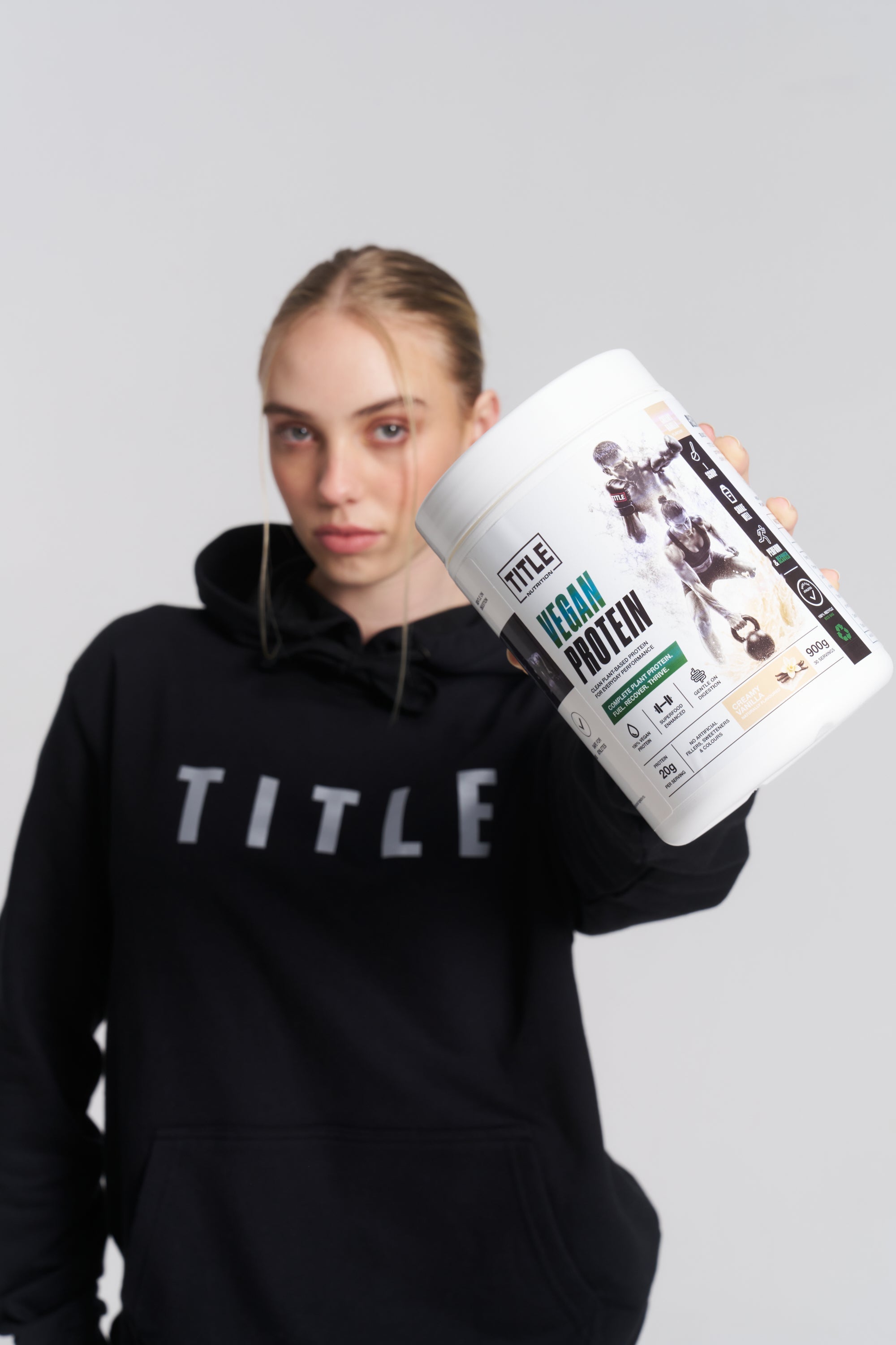 TITLE Boxing South Africa vegan protein powder tub held by a woman wearing a black branded hoodie
