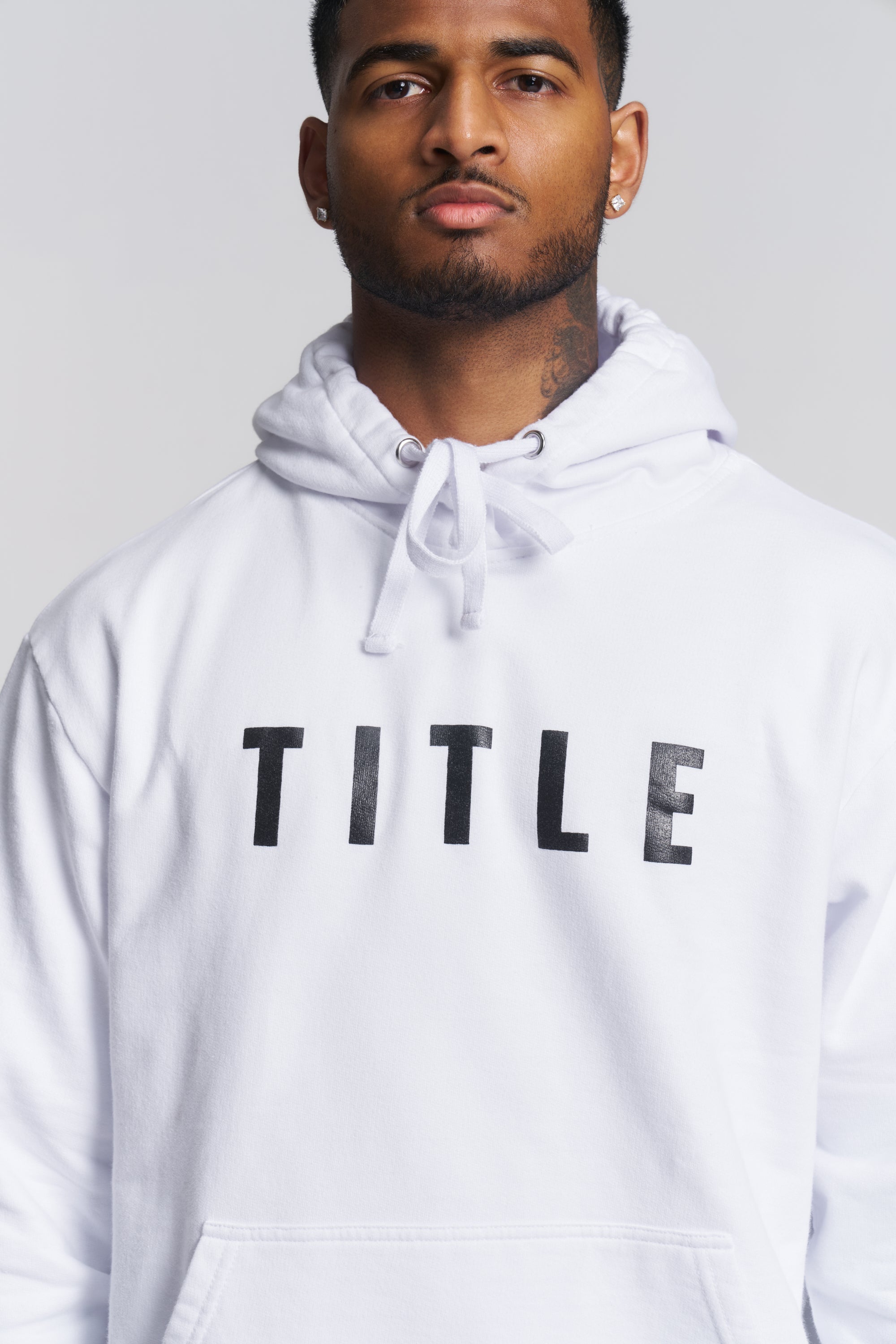 A man wearing a white pullover hoodie with the word 'TITLE' printed in black across the chest, photographed against a light gray studio background.
