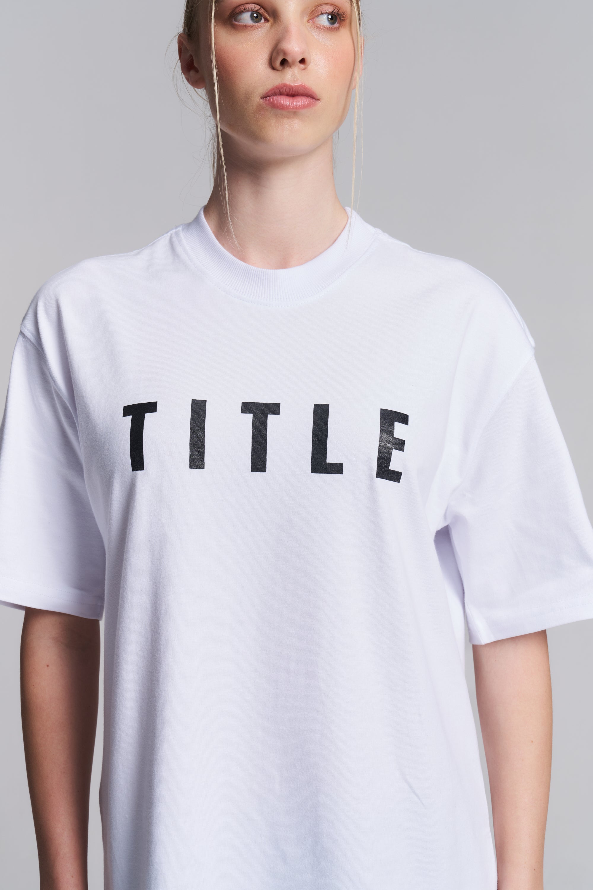 Model wearing a white TITLE Boxing South Africa oversized cotton t-shirt with black chest logo and mock-neck collar