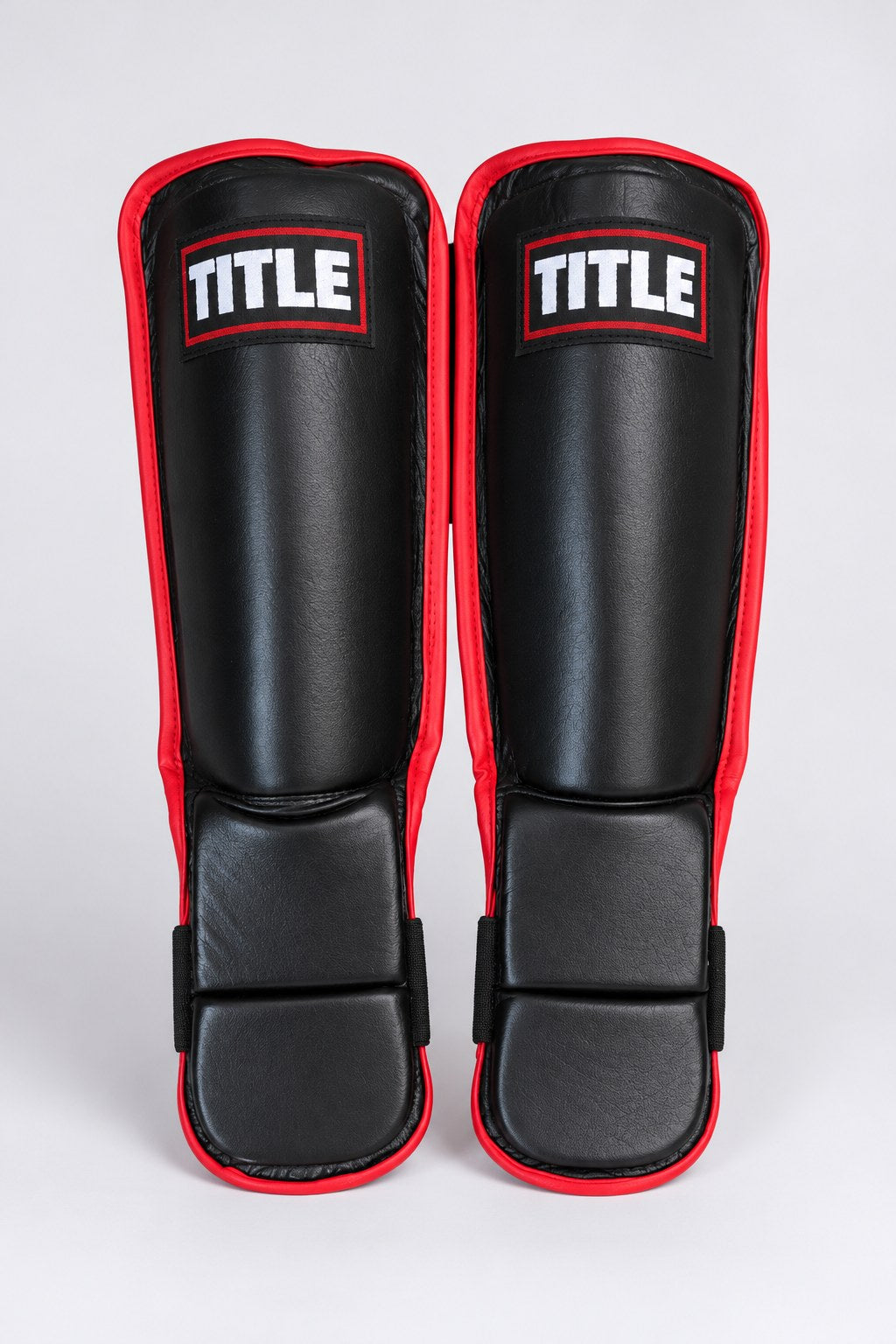 TITLE Defender leather shin guards in black with red trim, front view with TITLE patch and two-section instep