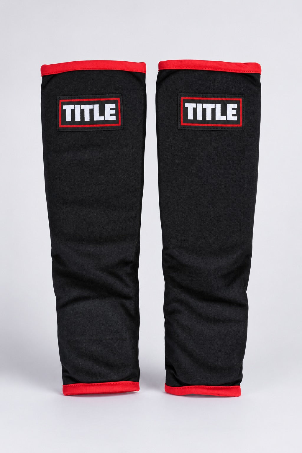 TITLE Scramble elasticated shin guards in black with red trim, front view showing the TITLE patch on each shin