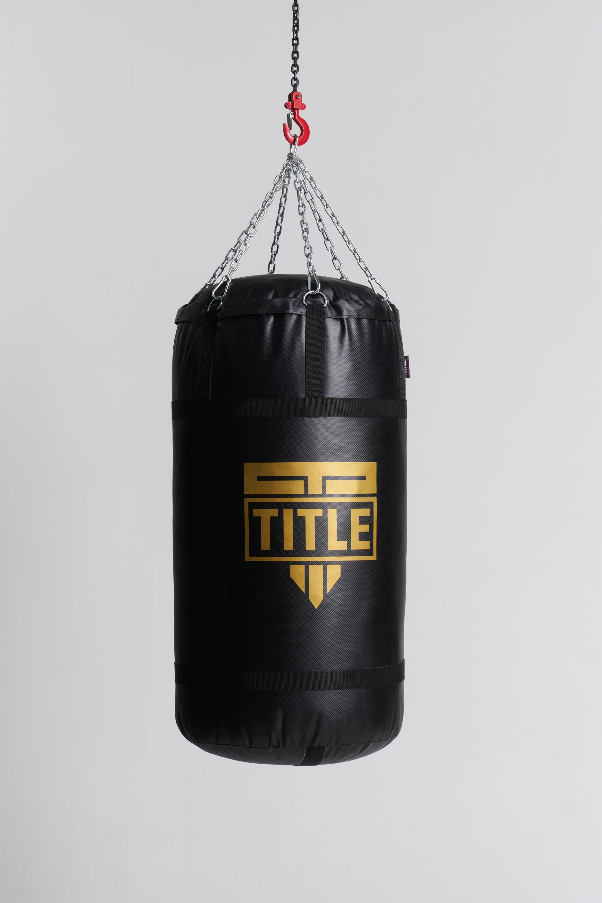 A black heavy punching bag hanging from a chain and hook, featuring a large gold TITLE logo on the front, set against a plain light gray background.