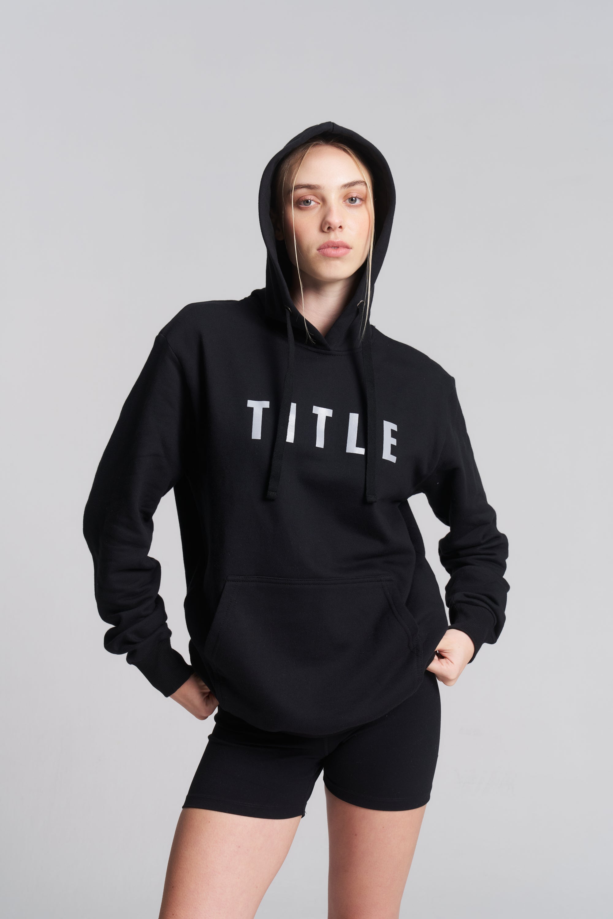 A model wearing a black TITLE Boxing South Africa heavyweight cotton hoodie with a grey chest logo and hood up.