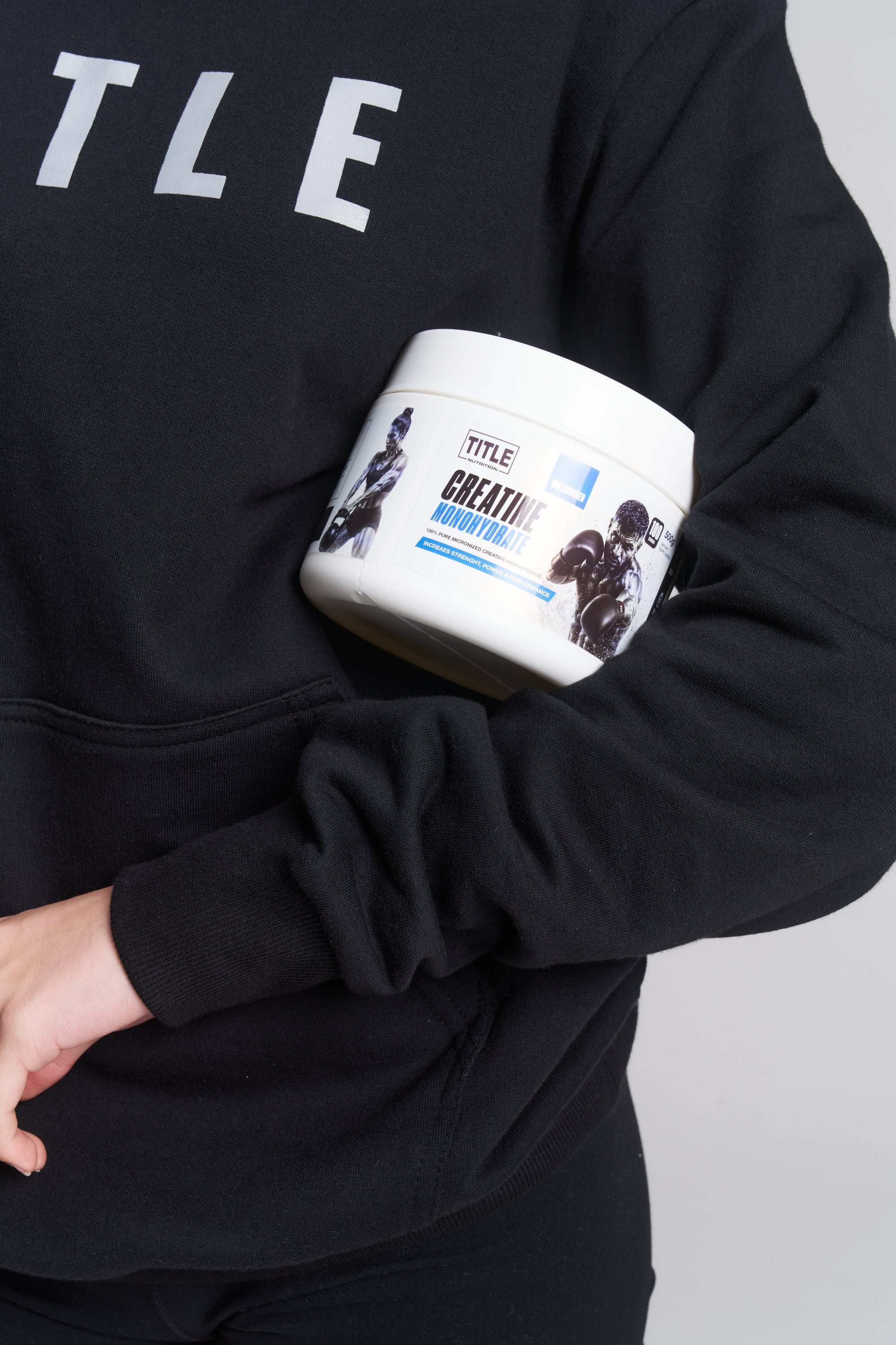 Person in black TITLE Boxing South Africa hoodie holding a 500g tub of TITLE Boxing South Africa Creatine Monohydrate