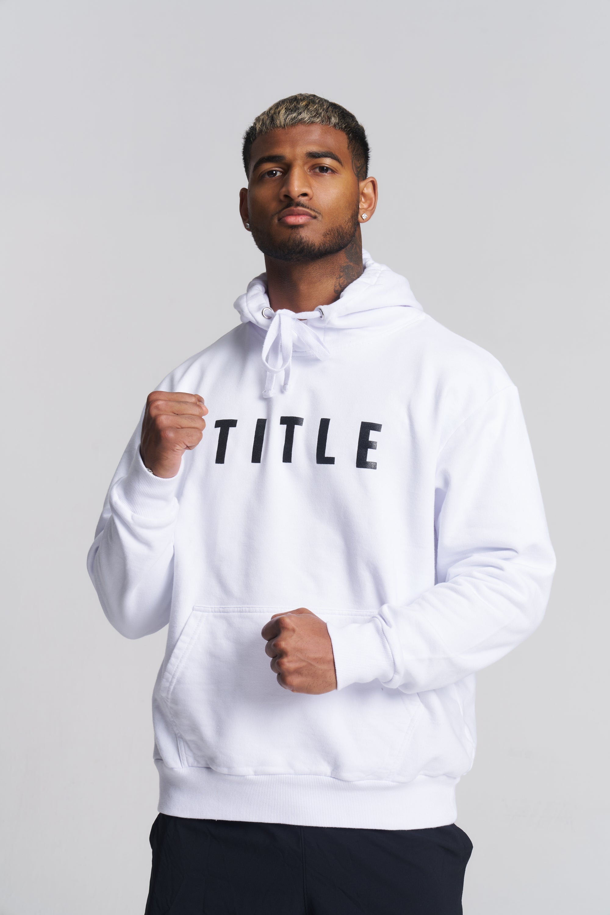 A man wearing a white pullover hoodie with the word 'TITLE' printed in black across the chest, posed against a light gray studio background.