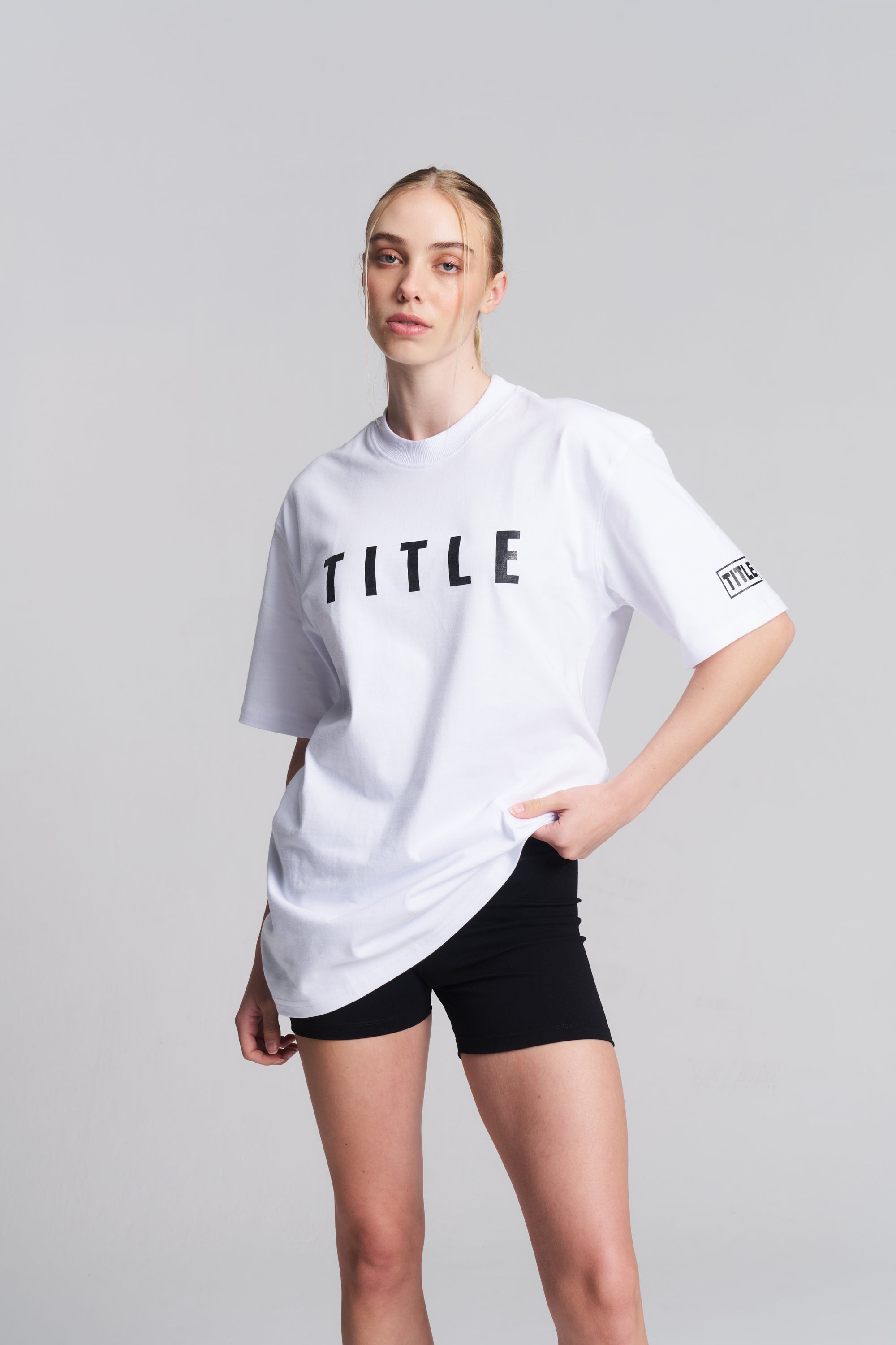 Model wearing a white TITLE Boxing South Africa oversized cotton t-shirt with black chest logo and sleeve detail