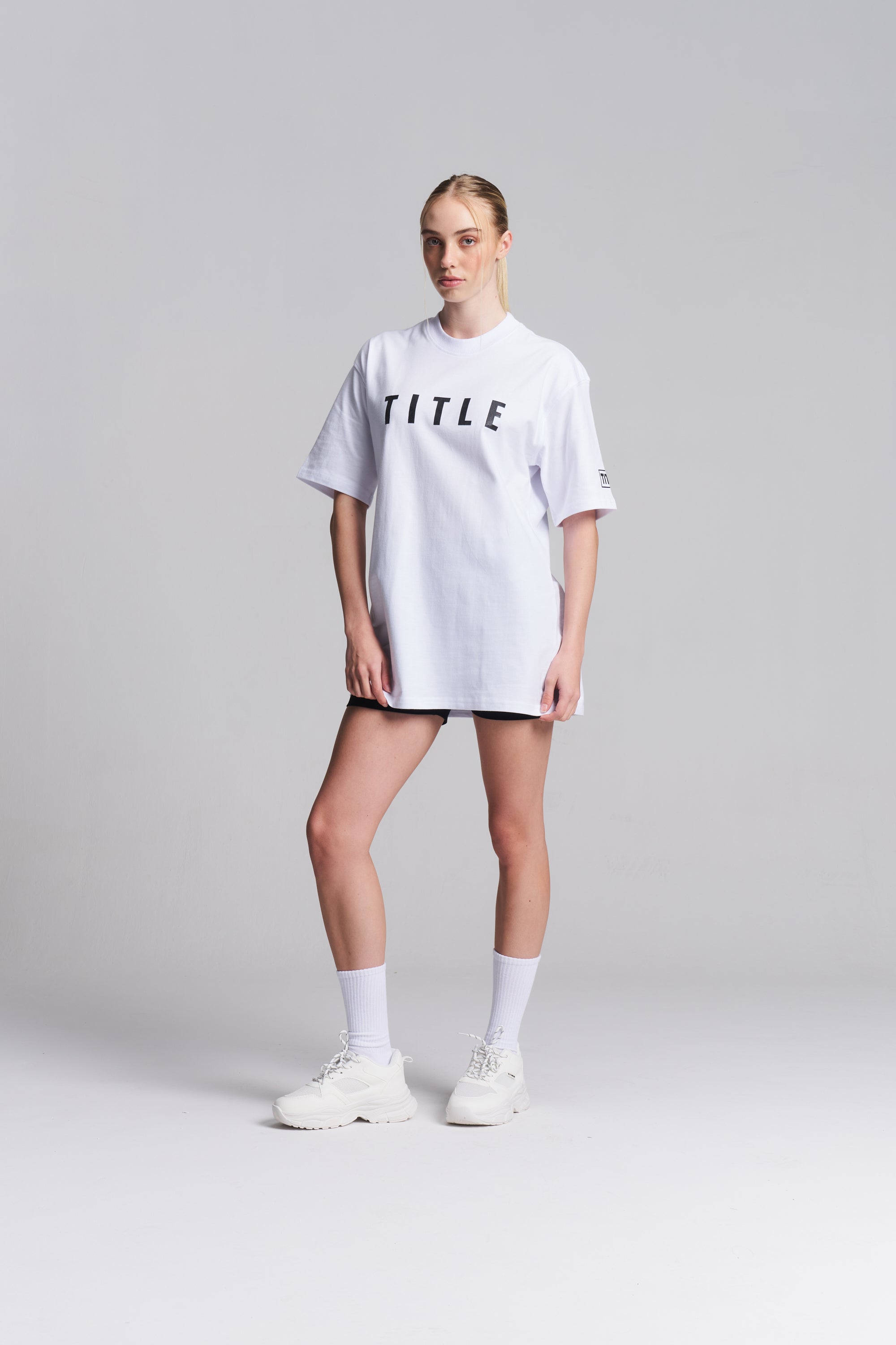 A model wearing a white TITLE Boxing South Africa oversized cotton t-shirt with black chest branding and mock-neck.